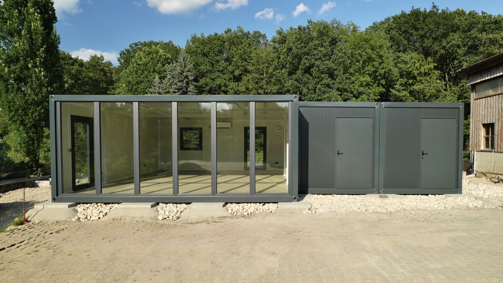 Anthrazit Mehrfachanlage mit Glasfront und angrenzenden Modulen vor Waldkulisse